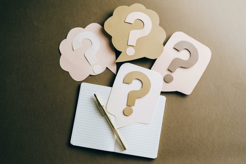 Icônes de points d’interrogation en papier au-dessus d’un carnet et d’un stylo, symbolisant les questions à poser avant de promouvoir un collaborateur manager.